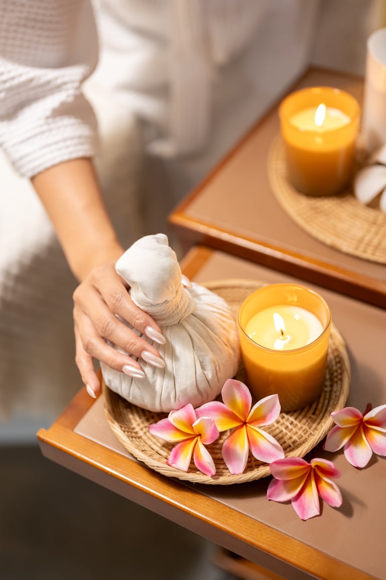 Woman hands holding herbal compress ball with candles and flowers in spa