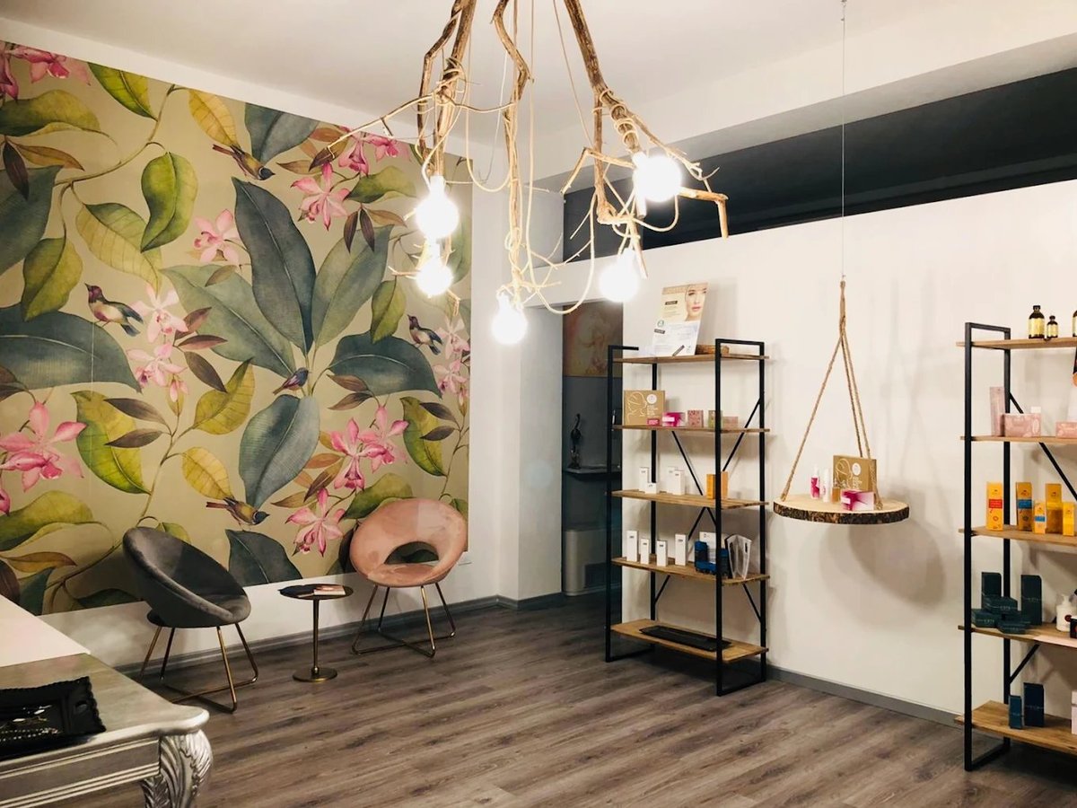 Modern interior space with tropical floral wallpaper, hanging plant, woven pendant lights, metal shelving, and mid-century furniture on wood flooring