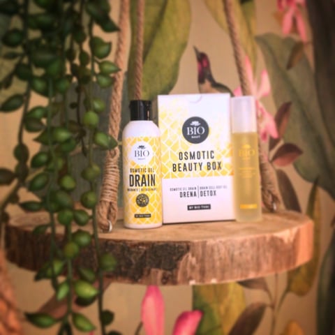 Bio skincare products displayed on wooden shelf with hanging green and pink plants in background